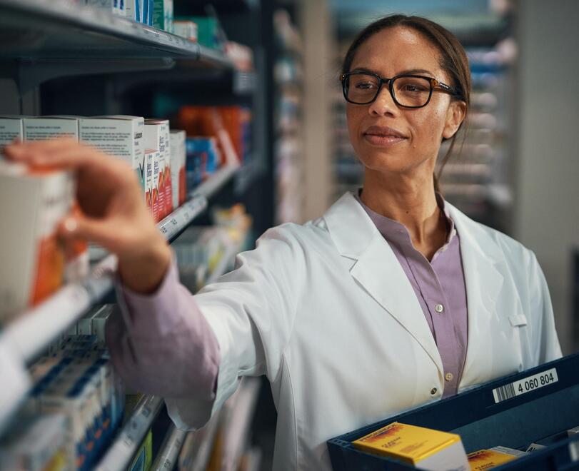 Pharmacist puts medication away, delivery box in hand
