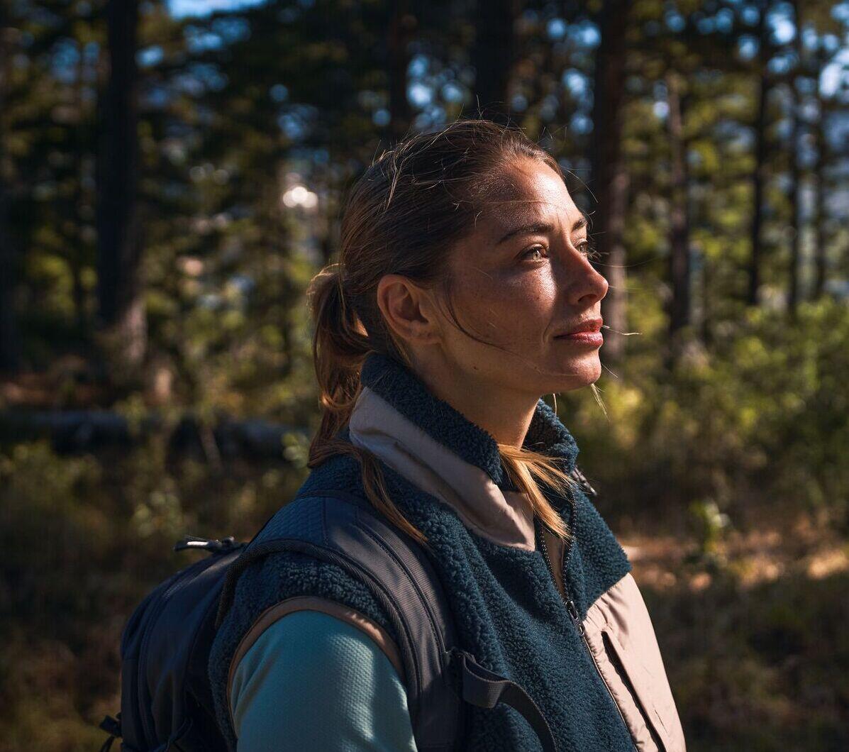 Eine Frau steht im Wald und schaut nachdenklich in die Zukunft