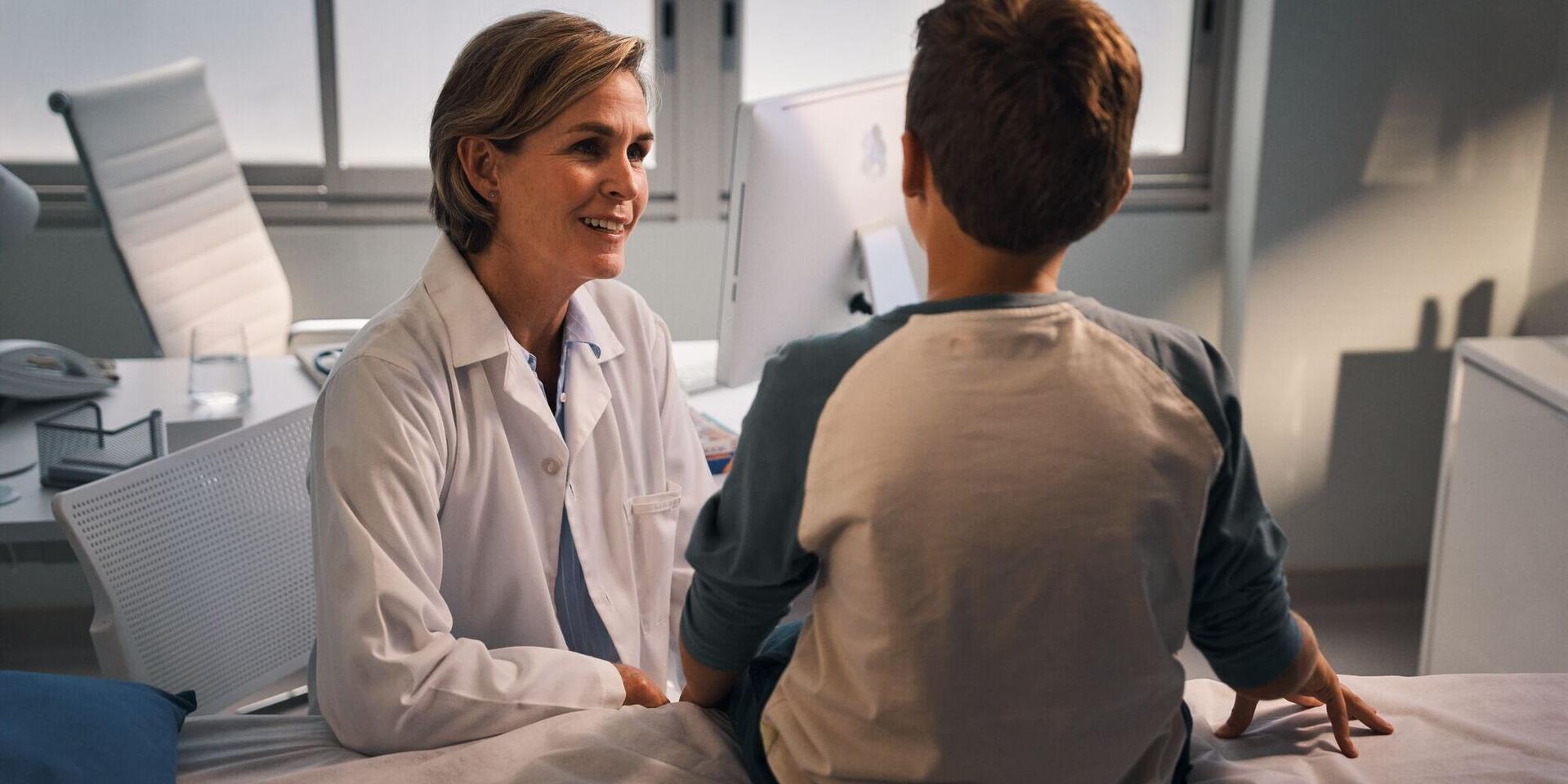 A doctor kneels in front of a boy and speaks to him with a smile